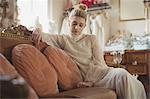 Thoughtful young bride in a white dress sitting on sofa in a boutique