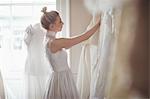 Young bride selecting wedding dress from clothes hanger in a boutique