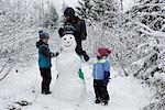 Happy family of three making snowman on snowy field