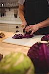 Midsection of male chef cutting red cabbage on cutting board in commercial kitchen