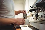 Midsection of male barista pouring milk into coffee cup at cafe