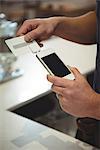 Cropped image of barista swiping credit card into device that is connected to mobile phone at cafe