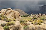 Rock formations of the Alabama Hills with storm clouds over the Sierra Nevada Mountains in the background in Eastern California, USA