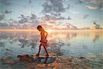 Girl wading in ocean surf on tranquil sunset beach