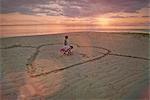 Boy and girl brother and sister drawing heart-shape in sand on tranquil sunset beach