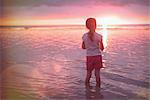 Pensive girl wading in ocean on tranquil sunset beach