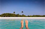 Personal perspective barefoot man floating in tropical ocean with beach view