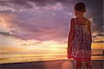 Pensive girl watching tranquil sunset in dramatic sky over ocean