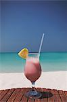 Pink cocktail with pineapple slice and straw on sunny tropical ocean beach