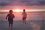 Boy and girl brother and sister on tranquil sunset beach with dramatic sky