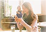 Woman texting with cell phone at cafe table