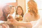 Smiling women friends toasting beer glasses in sunny bar
