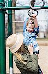 Girl hanging on climbing frame in mother's arms