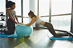 Two young women exercising in gym, using inflatable exercise ball