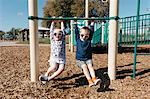 Boy and girl hanging from playground climbing frame