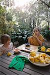 Two young sisters tasting and preparing lemons for lemonade at garden table