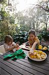 Two young sisters preparing lemons for lemonade at garden table