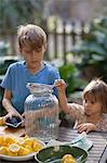 Boy and two young sister preparing lemon juice for lemonade at garden table