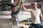 Two men high fiving in boat repair workshop