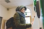 Woman in knit hat using touchscreen on railway ticket machine