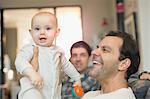 Portrait happy male gay parents holding baby son in living room