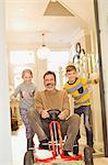 Portrait smiling children pushing father on toy car in foyer corridor