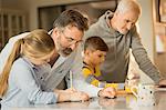 Male gay parents helping children doing homework at counter