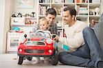 Male gay parents and baby son playing with toy car