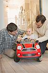 Male gay parents and baby son playing with toy car