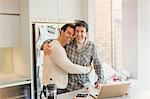 Portrait affectionate male gay couple hugging at laptop in kitchen