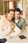 Portrait smiling, affectionate male gay couple with digital tablet hugging