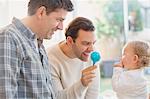 Male gay parents and baby son playing with rattle