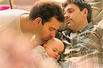 Affectionate male gay parents kissing sleeping baby son