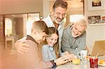 Male gay parents and children using cell phone at kitchen counter