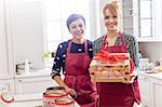 Portrait smiling female caterers showing wrapped box of pastries in kitchen