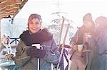 Portrait smiling female skier drinking coffee on cabin deck with friends apres-ski