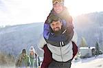 Portrait playful couple piggybacking in sunny, snowy field