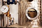 Close up of a gauge on a copper beer distillery chamber or fermentation tank. A round window to view contents