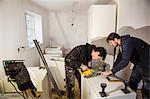 Two builders, cutting plasterboard for a kitchen unit with a circular saw.