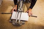 A builder, tiler kneeling on the floor, cutting a tile.