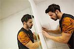 A builder, tiler placing tiles on a wall next to a mirror.