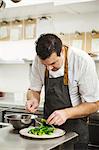 Chef standing in the kitchen in a small hotel, plating up a dish of vegetables.