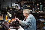 A grey haired senior worker, a woman sitting at a sewing machine in a shoemaker's workshop.