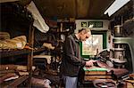 Man standing in a shoemaker's workshop, cutting brown leather.