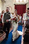 Smiling bride and groom walking down the isle in a church.