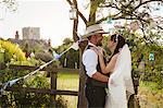 Newlywed couple, a bride and groom standing by a stile, hugging and gazing at each other.