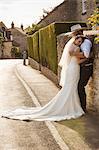 Newlyweds standing outdoors on a pavement, hugging and smiling.