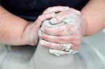 A person using a spinning pottery wheel to throw a pot using clay, hands pressing the wet clay into a basic shape for moulding on the turning wheel.