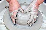 A person using a potter's wheel, throwing a clay pot and using thumbs to shape the wet clay. Seen from above.