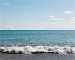 A sandy beach and waves breaking on the shore, and view to the horizon. Light wispy clouds.